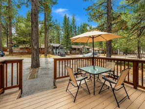 A wooden deck with a table and chairs, overlooking a residential area with houses and parked cars.