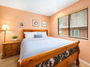 Une chambre à coucher avec un lit en bois, une table de chevet avec une lampe et une fenêtre avec des stores.