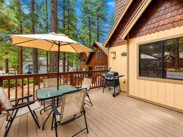 A deck with a table and chairs, an umbrella, and a grill.