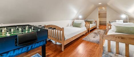 A cozy attic bedroom with a foosball table, two single beds, and a wooden ceiling.