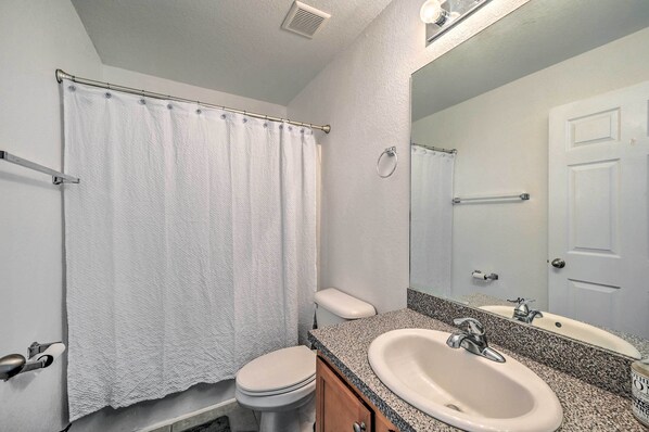 A bathroom with a white toilet, a sink with a granite countertop, and a shower curtain.