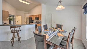 A modern kitchen with a central island, wooden chairs, and a dining table set for four. - Ranch-Style Lehigh Acres House with Big Backyard! (Lehigh Acres)