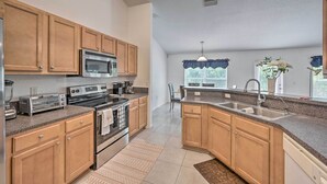 A modern kitchen with wooden cabinets, a stainless steel refrigerator, a microwave, a stove, and a large island with a sink. - Ranch-Style Lehigh Acres House with Big Backyard! (Lehigh Acres)