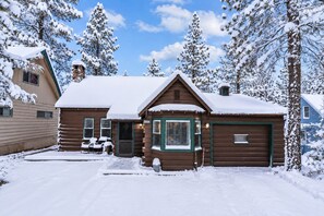 Una cabaña con techo nevado, un garaje y un camino de entrada que conduce a un vehículo.