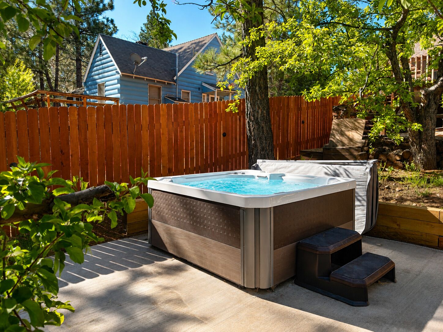 Un jacuzzi dans un jardin, avec une clôture en bois, des arbres et une maison en arrière-plan.