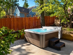 A hot tub in a backyard with a wooden fence, trees, and a house in the background.