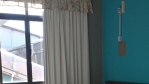 A hotel room with a large bed, a window with curtains, a wooden headboard, and a wall-mounted light fixture. - Ilha Azul Hospedagem (Florianópolis)