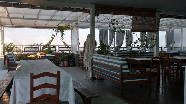 An outdoor dining area with tables and benches, potted plants, and a view of the sea. - Ilha Azul Hospedagem (Florianópolis)