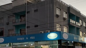 A building with a blue storefront labeled "Queijos & Paes" and a visible crosswalk. - Ilha Azul Hospedagem (Florianópolis)
