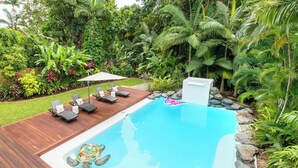 Une piscine avec une terrasse en bois, des chaises longues et une tortue dans l’eau.