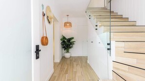 Un escalier moderne avec des marches en bois et une rampe en verre, menant à une pièce où se trouve une plante en pot et un luminaire suspendu.