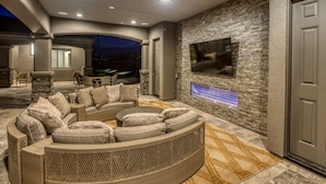 A modern outdoor living area with a curved sofa, stone pillars, and a flat-screen TV mounted on a stone wall.