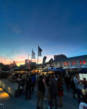 Ein belebtes Freiluft-Event mit Zelten und Flaggen vor einem Sonnenuntergangshimmel.