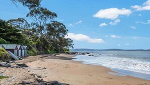 A beach with a sandy shore, a row of beach huts, and a clear blue sky. - Treetops-Large Home 9km to CBD Sleeps 10. (Taroona)