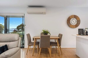 A modern living room with a dining area, a large wooden clock, and a view through a glass door.