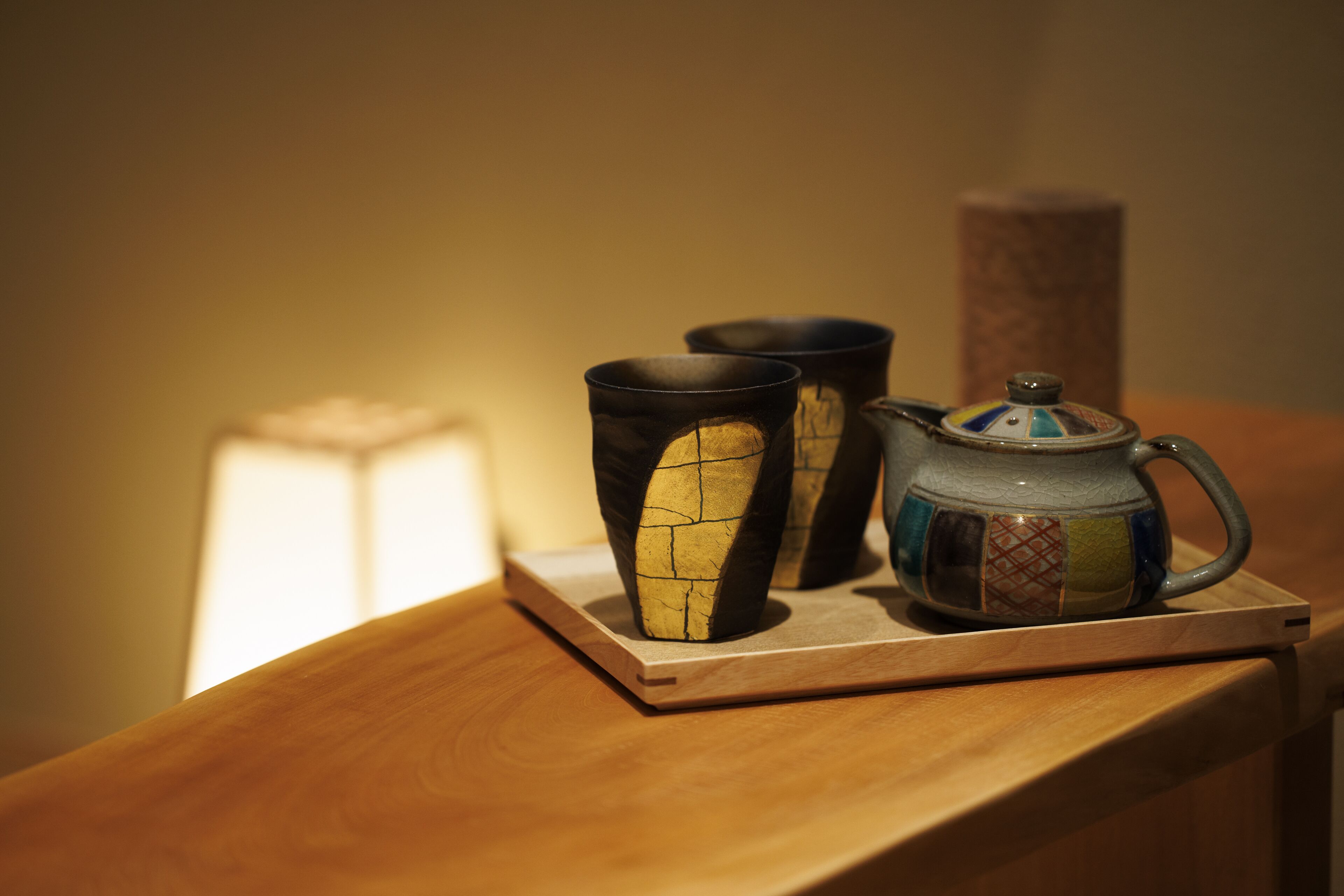 A wooden table with a ceramic mug and two cups on a coaster.
