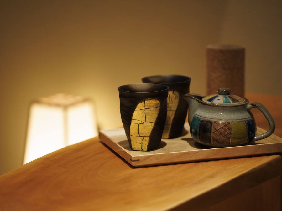 A wooden table with a ceramic mug and two cups on a coaster.