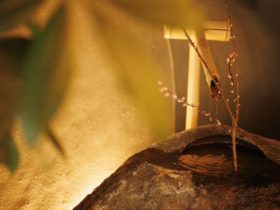 A rock basin with a branch of flowers and a wooden structure in the background.