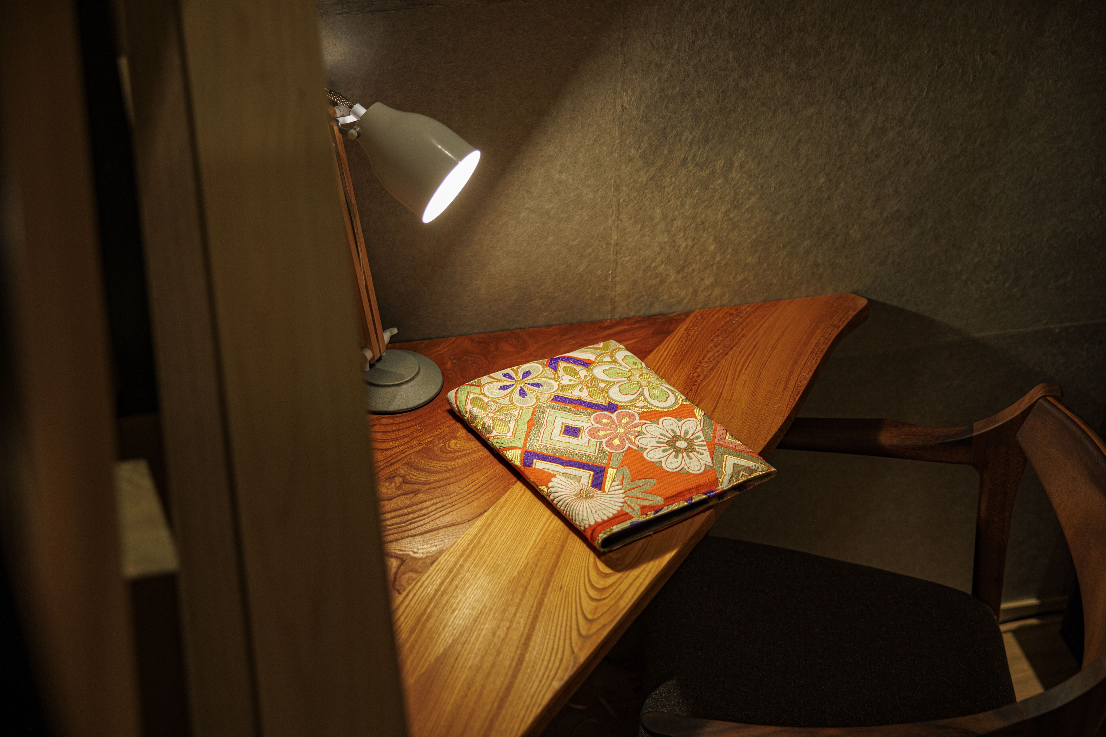 Ein Holztisch mit einem gemusterten Notizbuch, einer Schreibtischlampe und einem Stuhl.