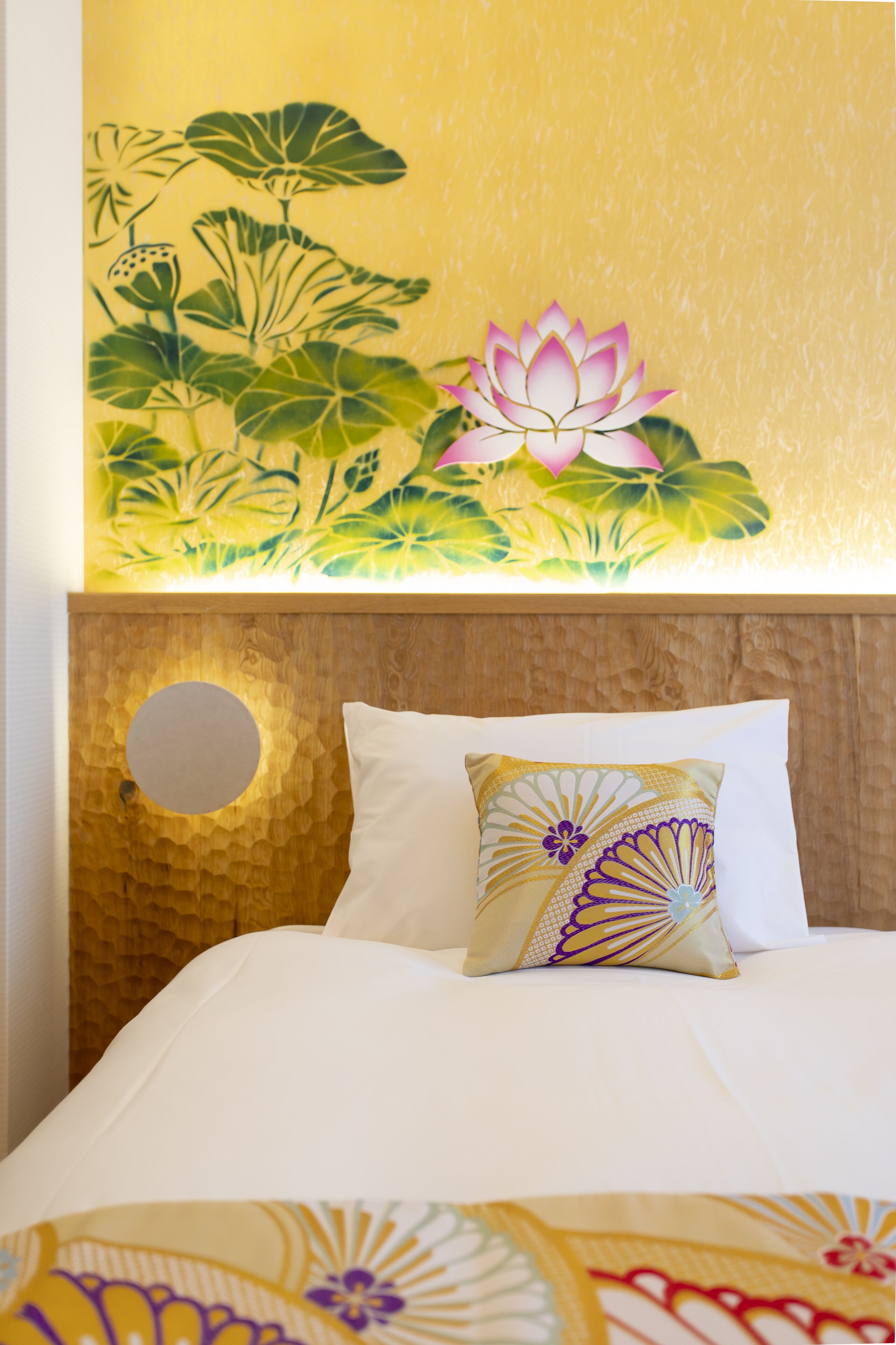 Una habitación de hotel con una cama, un almohadón con diseño floral y un mural de flores de loto.