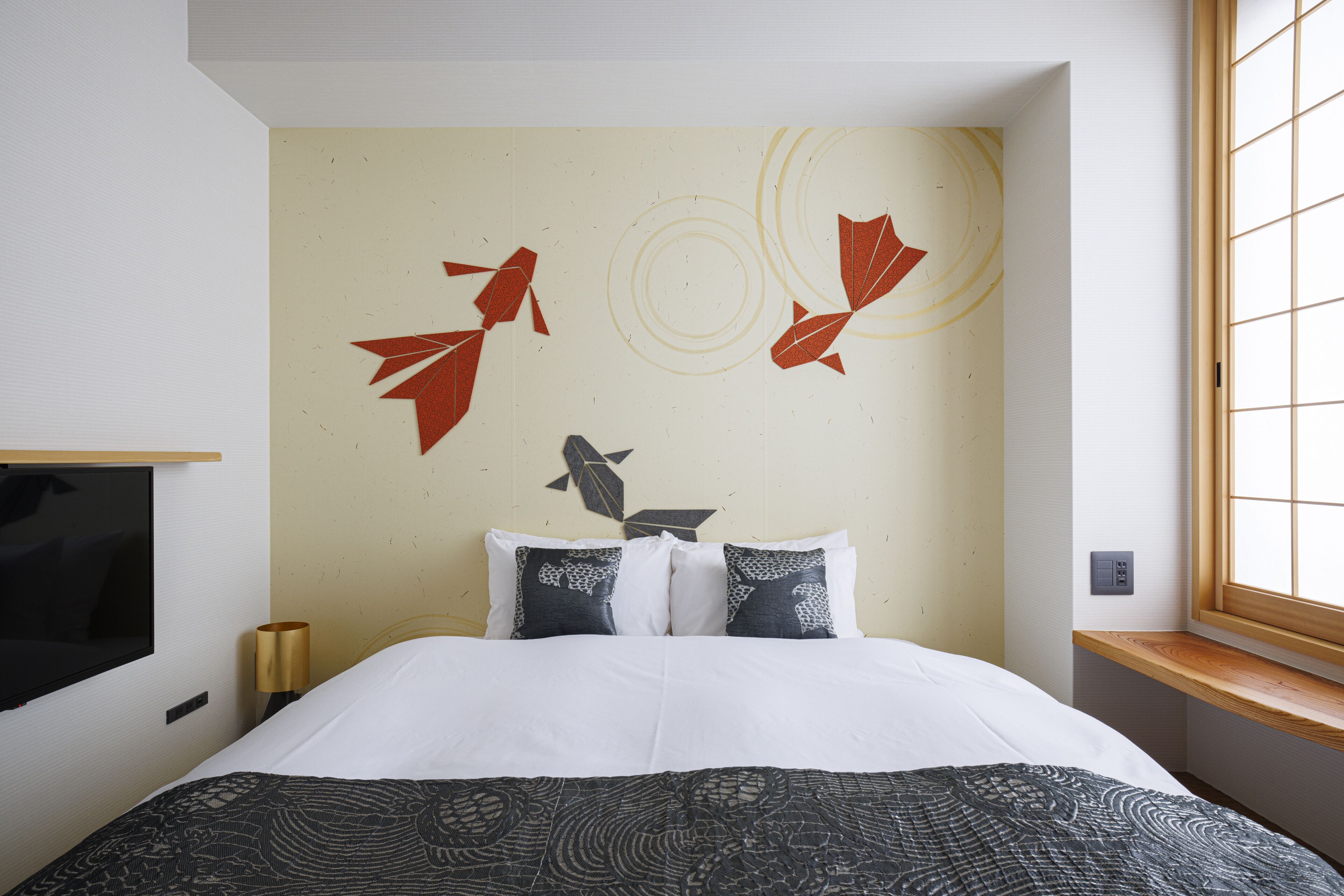 A hotel room with a bed, a TV, a window, and a wall with decorative leaf patterns.