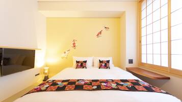 A hotel room with a bed, pillows, a quilt, a bedside table with a lamp, a TV, and a window with a view.