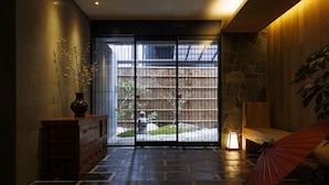 Una habitación con pared de piedra, un banco de madera, un paraguas rojo y un florero con ramas.