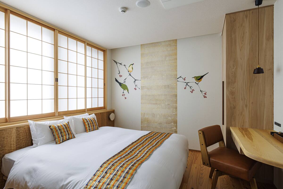 Habitación de hotel con una cama grande, un escritorio de madera y vistas a través de un fusuma.