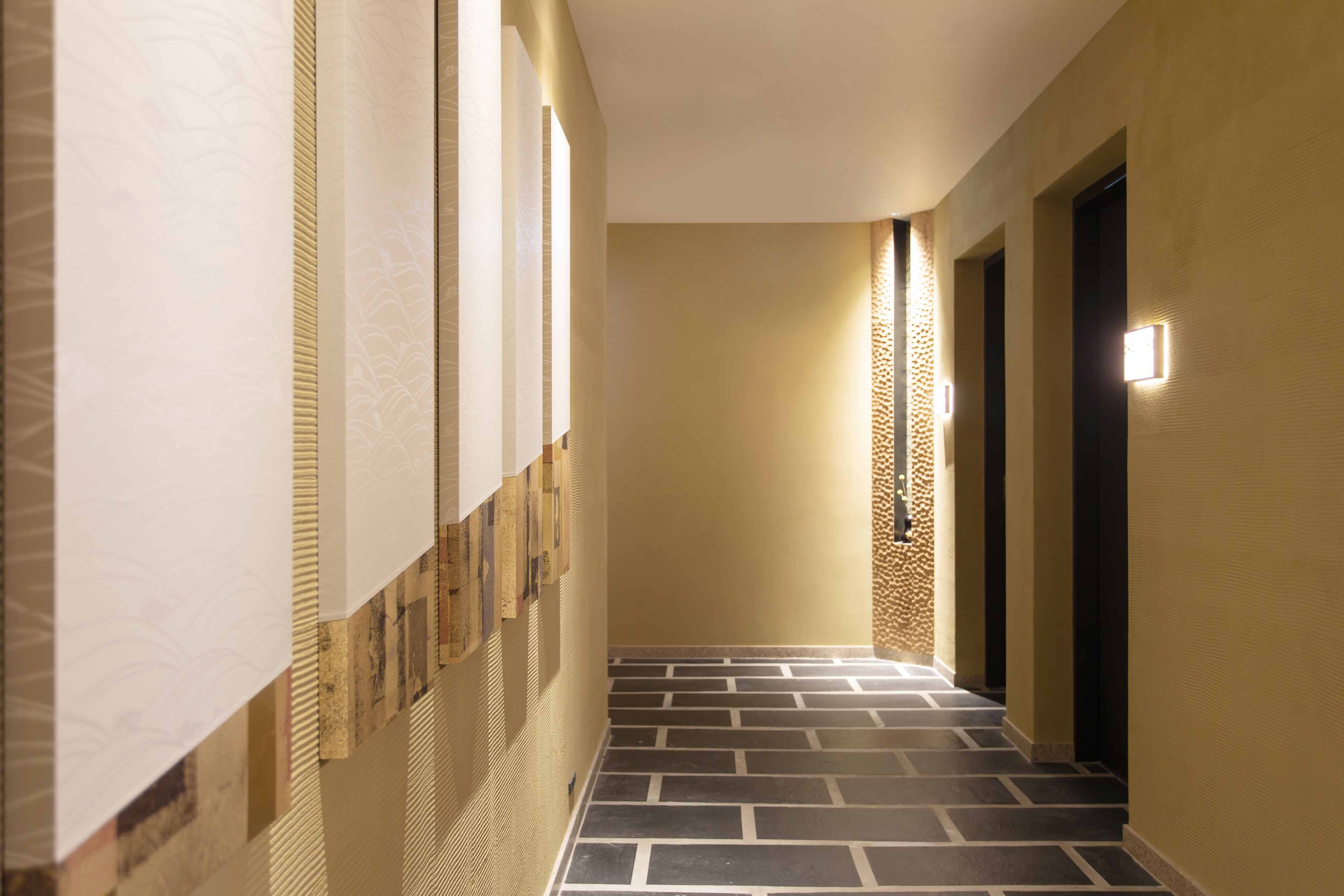 A hallway with patterned walls, a tiled floor, and a light fixture on the wall.