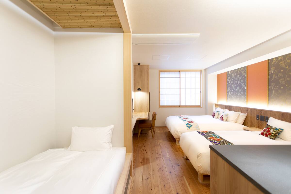Una habitación de hotel con dos camas, suelo de madera, un escritorio y un ventanal grande.