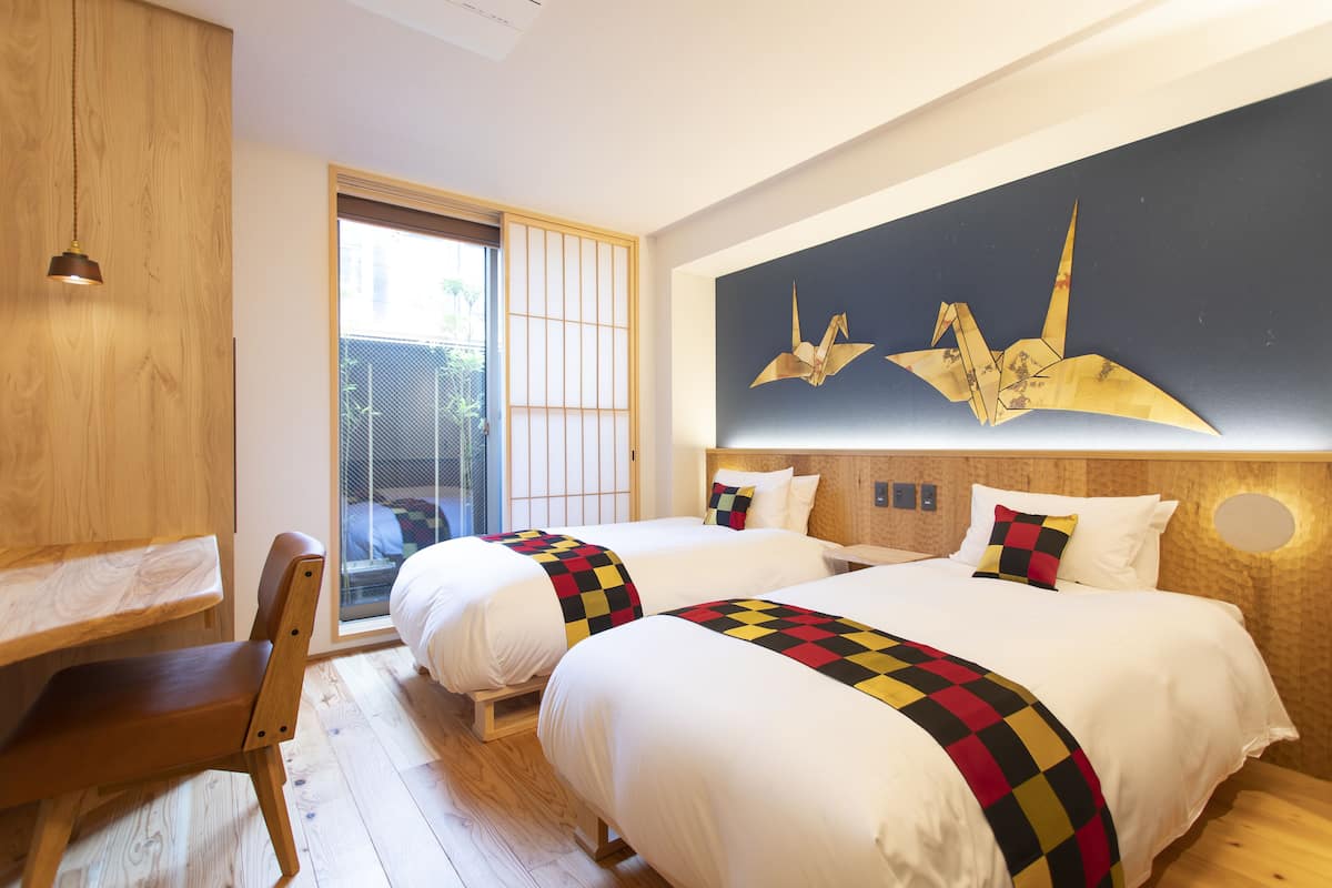 Habitación de hotel con dos camas, suelo de madera, un escritorio y una obra de arte grande en la pared.
