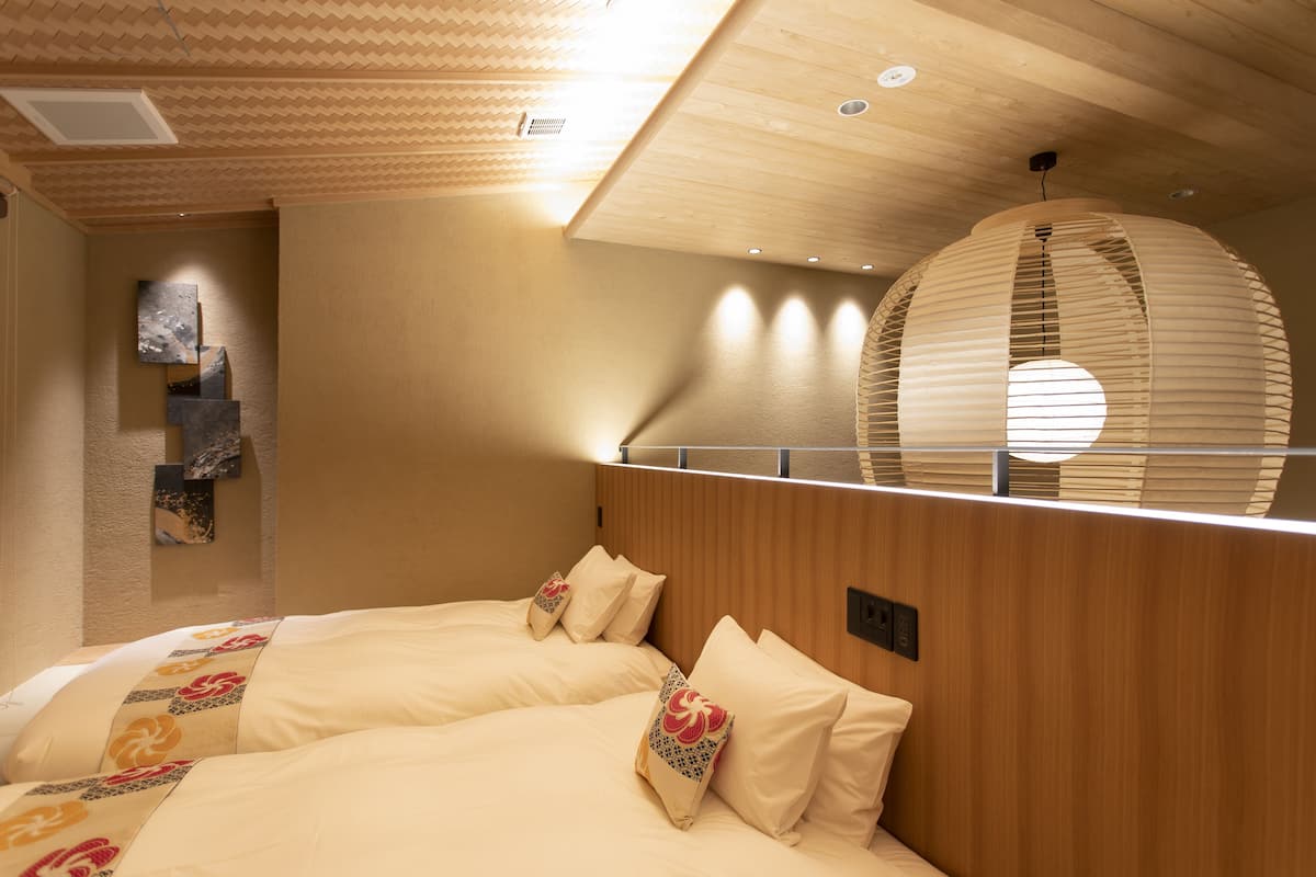 Habitación de hotel con dos camas, cabeceros de madera, un techo con diseño geométrico y una lámpara circular grande.