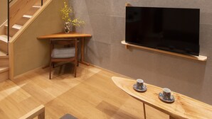 Un interior moderno con una escalera de madera, un televisor de pantalla plana en la pared, una pequeña mesa con dos tazas y una silla.