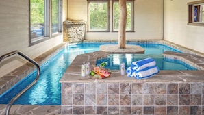 Une piscine intérieure bordée de pierres, dotée d’une terrasse en bois et d’un mur en pierre.