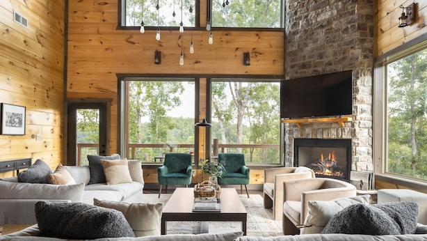 L’intérieur chaleureux d’un chalet, avec ses murs en bois, sa cheminée en pierre et ses grandes fenêtres donnant sur la forêt.