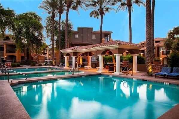 A swimming pool with clear water, surrounded by palm trees and a building with a tiled roof.