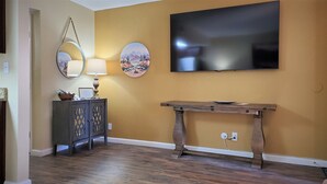 Una habitación con piso de madera, una consola de madera oscura, un televisor de pantalla plana montado en la pared y dos espejos redondos fijados a la pared.