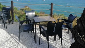 Terraza frente al mar con una mesa y sillas, con vista al océano y una barandilla de cuerda.