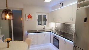 Una cocina moderna con armarios blancos, un refrigerador de acero inoxidable, horno empotrado y una lámpara colgante.