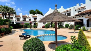 Una piscina con sombrilla de techo de paja, rodeada de edificios blancos con tejados de azulejos.