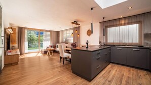 Une cuisine moderne dotée d’un îlot central, de meubles de rangement aux couleurs sombres et d’un coin repas avec une table et des chaises.