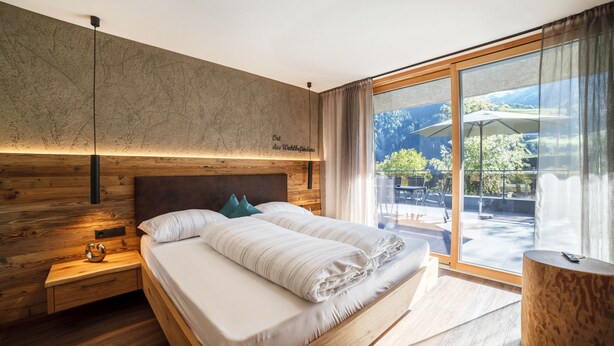 Une chambre moderne avec un grand lit, une tête de lit en bois et une vue sur l’extérieur.