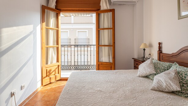 Une chambre à coucher avec un lit, des oreillers, une table de chevet et une fenêtre ouverte donnant sur l’extérieur.