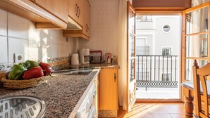Une cuisine avec des meubles en bois, un plan de travail en granit, un panier de poivrons, une machine à café et une vue sur un balcon.
