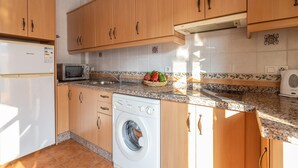 Une cuisine avec des meubles de rangement en bois, un lave-linge, un four à micro-ondes et un évier.