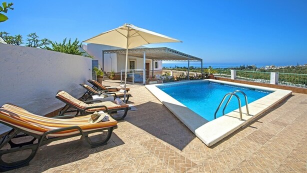 Zona junto a la piscina con sillones, piscina y vista al mar.