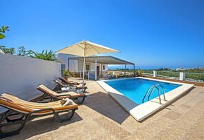 Zona junto a la piscina con sillones, piscina y vista al mar.