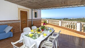 Una terraza con una mesa lista para comer, un sofá y vista al mar.