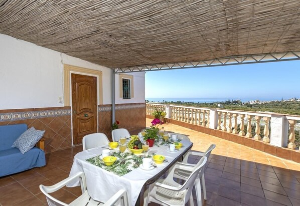 Una terraza con una mesa lista para comer, un sofá y vista al mar.