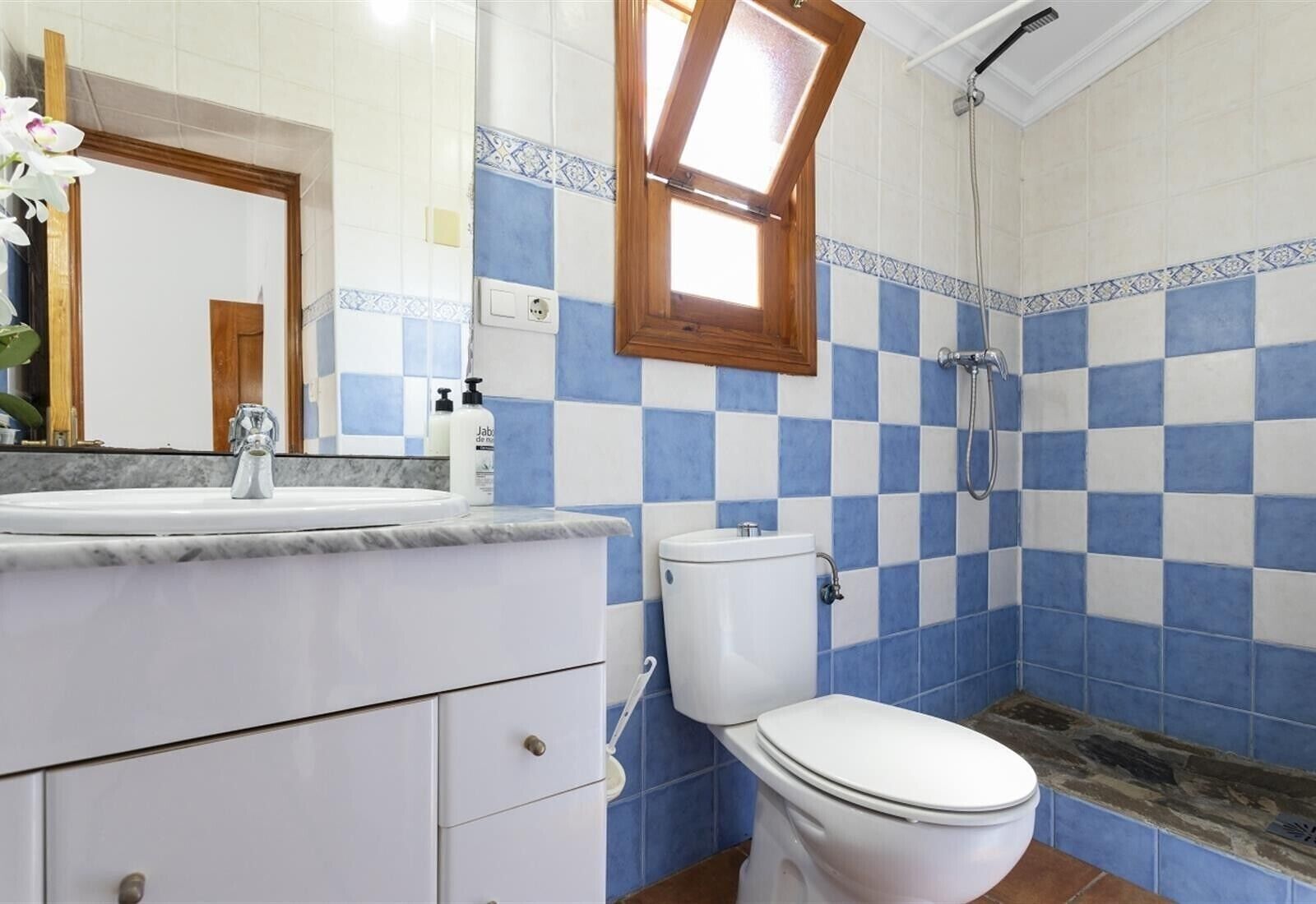 A bathroom with a checkered tile pattern, a white sink, a toilet, and a shower.